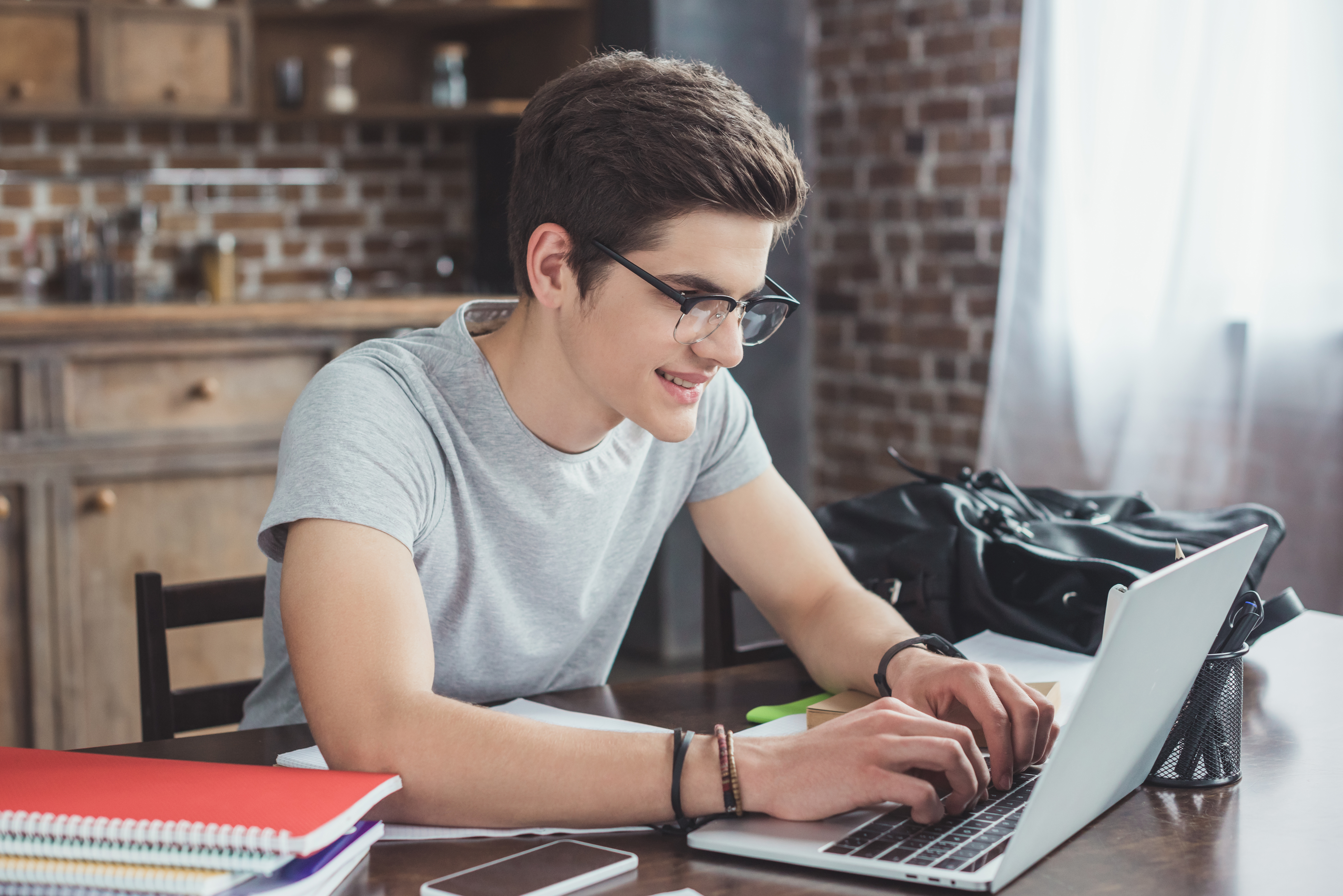 smiling student doing homework and typing on laptop
